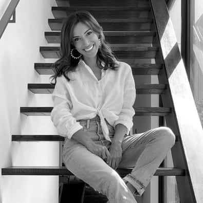 A woman sitting on stairs in a white shirt and jeans.